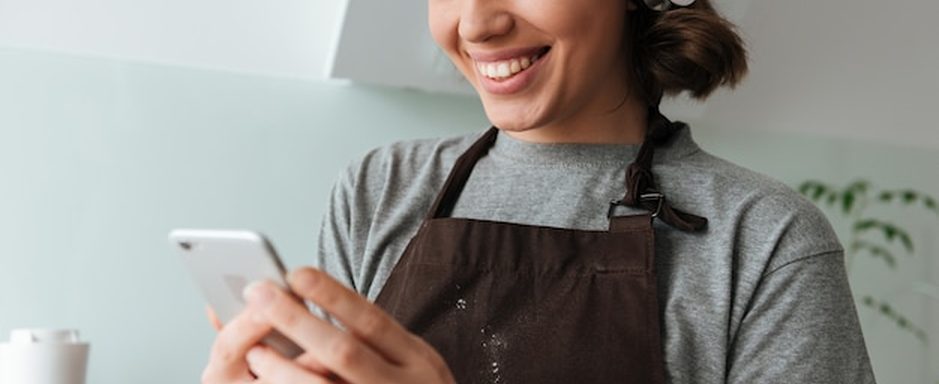 Dono de uma pequena loja olhando o celular com uma conversa de atendimento automatizada, balcão ao fundo